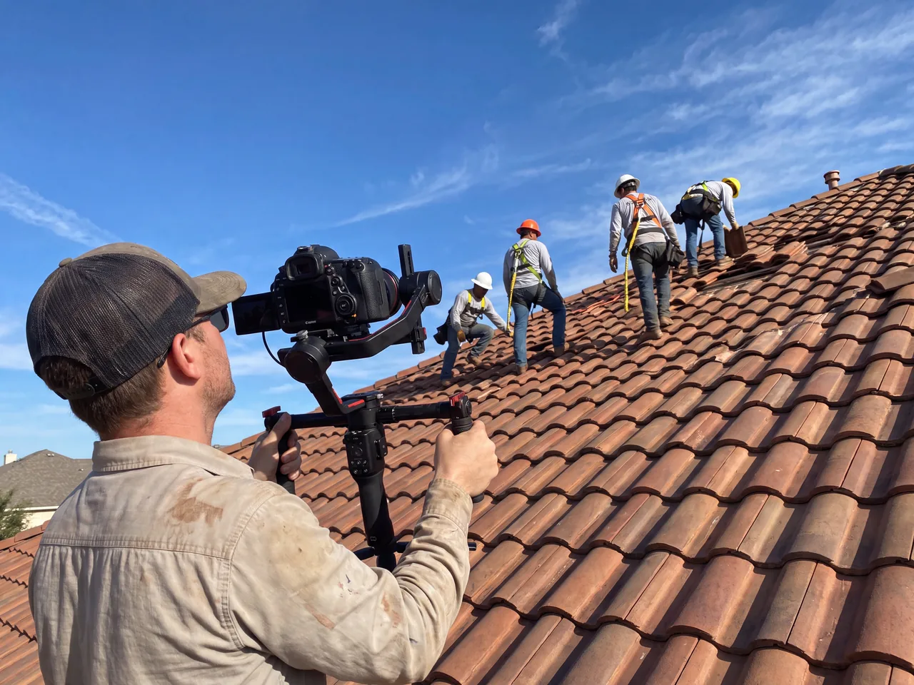 Videographer filming a roofing crew on a Spanish tile roof